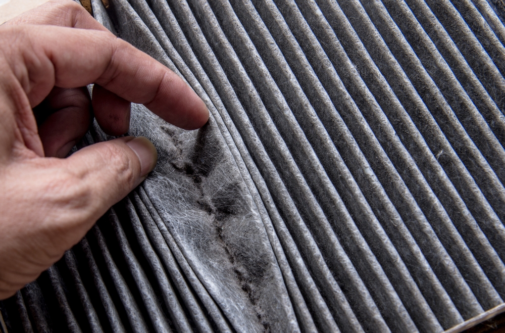 person inspecting an air filter with their finger, filter is very dirty