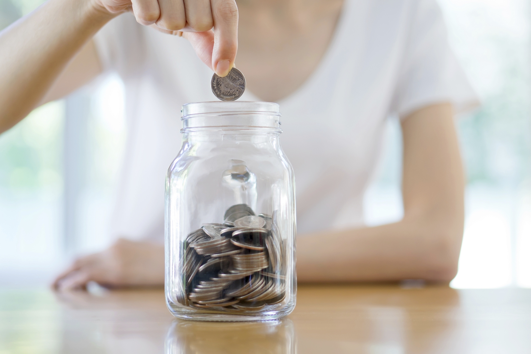 woman saving coins into a jar, saving money